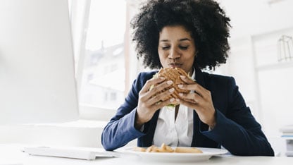 Joven mujer de negocios comiendo una hamburguesa en su escritorio